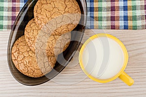 Round cookies in black dish and cup of milk on table