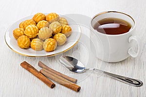 Round cookies in saucer, teaspoon, tea, cinnamon sticks on table