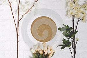 Round cork board and flowers on white brick background.