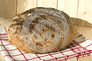 Round dark colored loaf on a white towel with red stripes. Belgian bread. Closeup