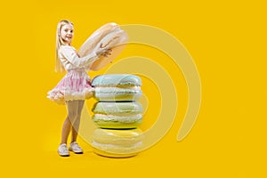 Round dessert. Sweet gift. A cute girl is holding a huge macaroon on a yellow background. Christmas sweetness