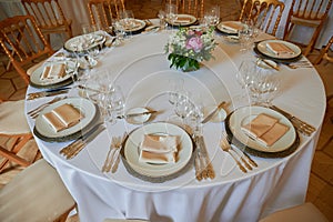 A round dining table with a white tablecloth and cloth napkins is prepared for a banquet for several persons