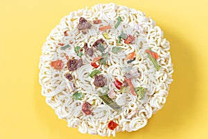 Round dry instant noodles with spices on yellow background, view from above