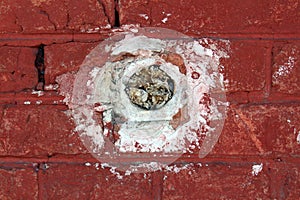 Round electrical outlet box without wires filled with paper mounted inside red brick wall