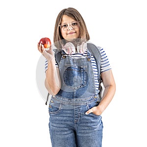 Round-faced girl in glasses and headphones on her neck holds a red apple in her hand