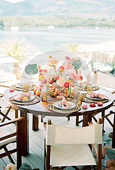 Round festive table with bouquets of flowers and plates on wicker rugs on the terrace overlooking the sea