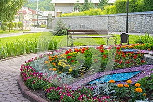 Round flower bed with colorful decorative flowers and plants, garden bench stands on the paving tiles, a beautiful recreation area