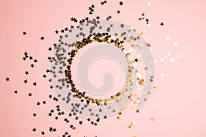 Round frame from golden star shaped glitter confetti on pink background. Festive flat lay holiday pastel backdrop with copy space