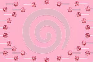 Round frame of lollipops with red and white stripes on a pink background