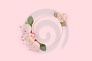Round frame made of green leaves and rose flowers on a pink background.
