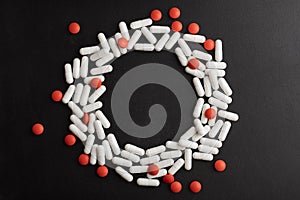 Round frame of pills, white capsules and red pills on a black background with place for text. Medicine, healthcare concept.