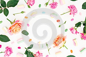 Round frame of Roses flowers and marshmallow with colorful candy on white background. Flat lay, top view.