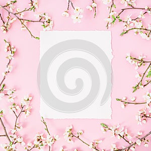 Round frame with spring flowers and white paper vintage car on pink background. Flat lay, top view.