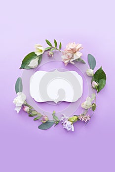 Round frame wreath with pink roses, white flowers, branches, leaves and petals on purple background. Flat lay, top view