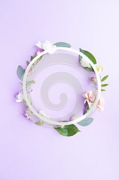 Round frame wreath with pink roses, white flowers, branches, leaves and petals on purple background. Flat lay, top view