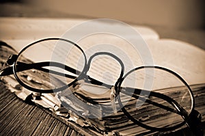 Round-framed eyeglasses and old book, in sepia toning