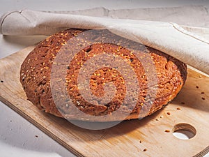 Round freshly baked homemade wholegrain bread loaf lies on a wooden kitchen board