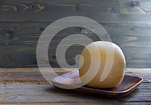 Round head of cheese Kostromskoy on textured dark wooden background on the square plate. Horizontal with copy space
