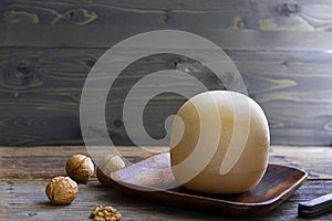 Round head of cheese Kostromskoy on textured dark wooden background on the square plate with several walnuts around