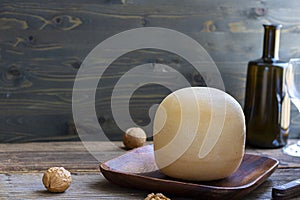 Round head of cheese Kostromskoy on textured dark wooden background on the square plate with walnuts and defocused