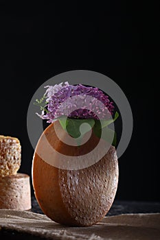 Round head of hard cheese with a sprig of lilac on a black background. Vertical photo. Copy of the space. The concept of still