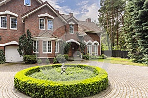 Round hedge and a small statue in the middle of a cobblestone dr