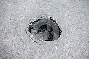 Round hole in gray asphalt, damaged road