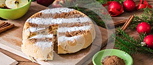 Round homemade cinnamon apple pie in a wicker plate on a wooden table with Christmas decorations around