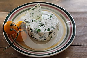 Round homemade fresh natural cheese lying on a plate next to the tomato on a wooden table.
