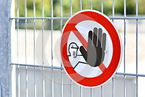 Round `Keep out` warning sign with person holding up hand in red circle at fence protecting construction site