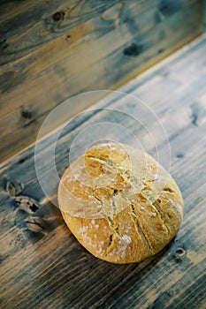 Round loaf of bread lies below on a wooden table. Top view