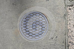 Round manhole cover witj a diamond pattern on the sidewalk