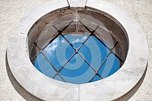 Round medieval window with bars blue sky view - Abstract Concept Background - Indoors Outdoors Concept - Round window with window