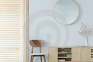 Round mirror above wooden chair and cabinet in minimal anteroom interior with decor