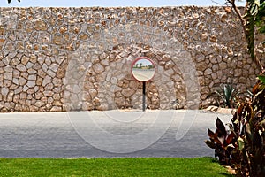 Round mirror on the background of the old stone wall and the road