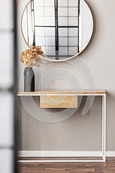 Round mirror in wooden frame above fancy console table with flowers in vase in trendy bedroom interior with beige vase