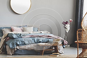 Round mirror in wooden frame above king size bed with blue, beige and pastel pink bedding