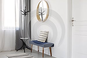 Round mirror in wooden frame on empty white wall of bright living room interior