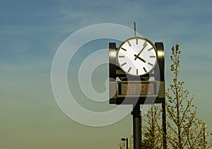 Round outdoor clock with electronic thermometer against the blue sky
