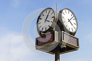 Round outdoor clock with electronic thermometer against the blue sky
