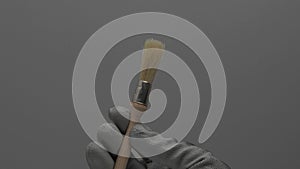 A round paint brush rotates in a hand on a gray background.