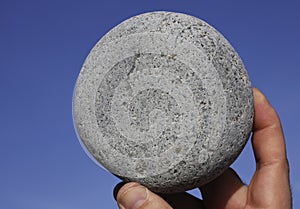 round pebble stone hold in male hand on blue sky background