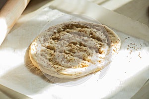 Round piece of dough on a table, preparing Ramadan pide with sesame seeds