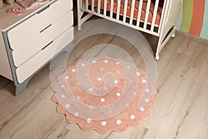 Round pink rug with polka dot pattern on floor in baby`s room, above view