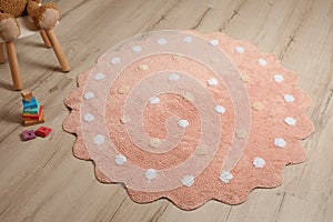 Round pink rug with polka dot pattern and toys on floor in baby`s room