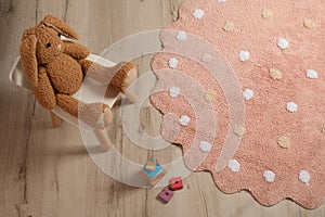 Round pink rug with polka dot pattern and toys on floor in baby`s room, above view
