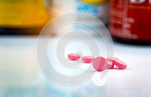 Round pink tablets pill on blurred background of drug bottle. Painkiller medicine. Drug use for treatment migraine headache.