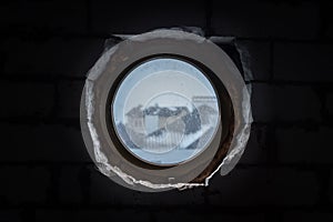 Round plastic window in a bunker with bare walls in the dark overlooking private houses