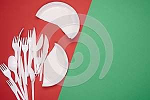 Round plate and stack of plastic forks and spoons on red background, top view