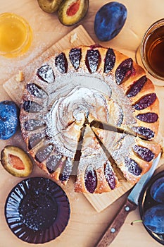 Round plum cake decorated with icing sugar, a cup of black tea and a saucer with fruit